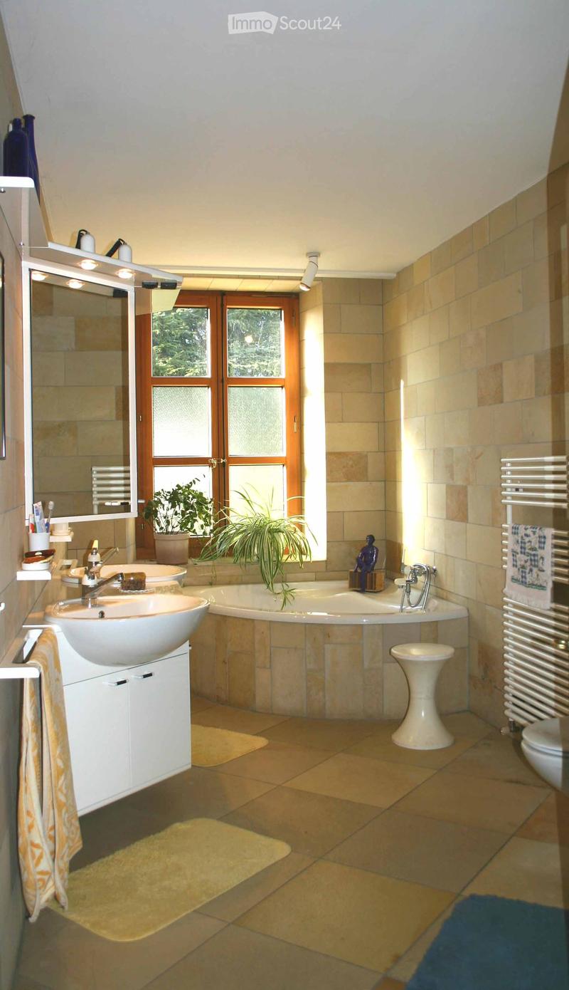 Modern bathroom with beige tiles, a large window, a sink with a mirror, a bathtub, a white stool, a radiator, and a small plant on the windowsill.
