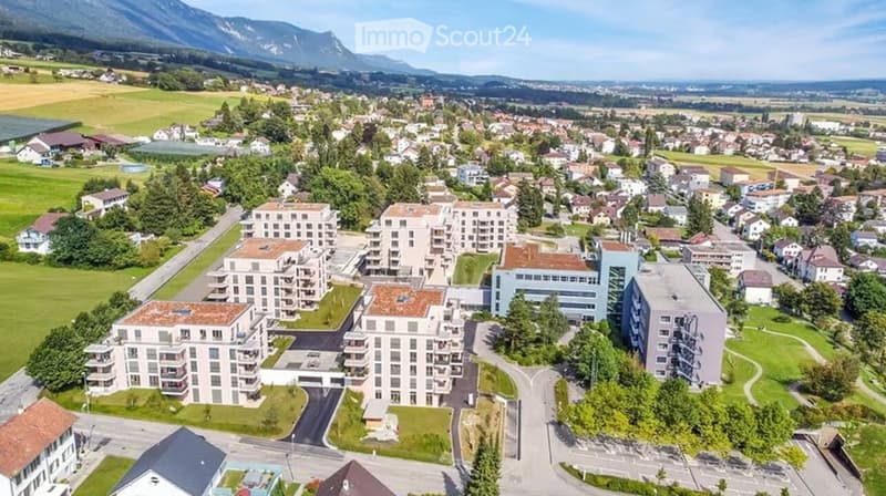 Aerial view of a residential area with multiple modern apartment buildings, surrounded by green spaces and a scenic mountain backdrop.