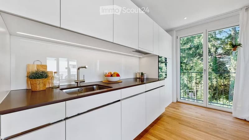 Modern kitchen with white cabinets, wooden countertop, stainless steel sink, and a large window with a view of greenery.