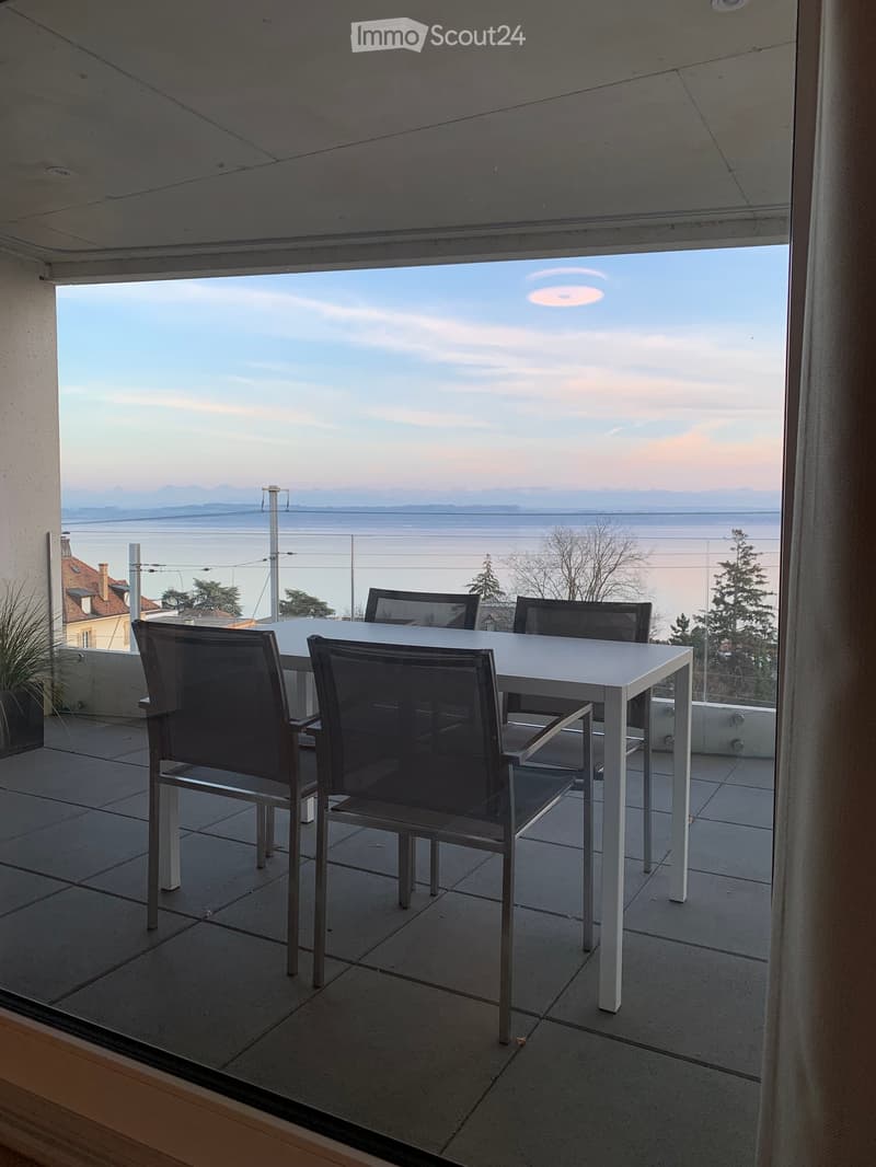 Balcony with a white table and four black chairs, overlooking a scenic view of water and distant mountains.