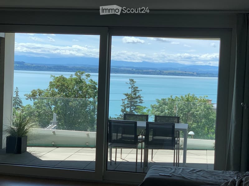 Balcony with a scenic view of a lake and mountains, featuring a small table and chairs, and a potted plant on the adjacent balcony.