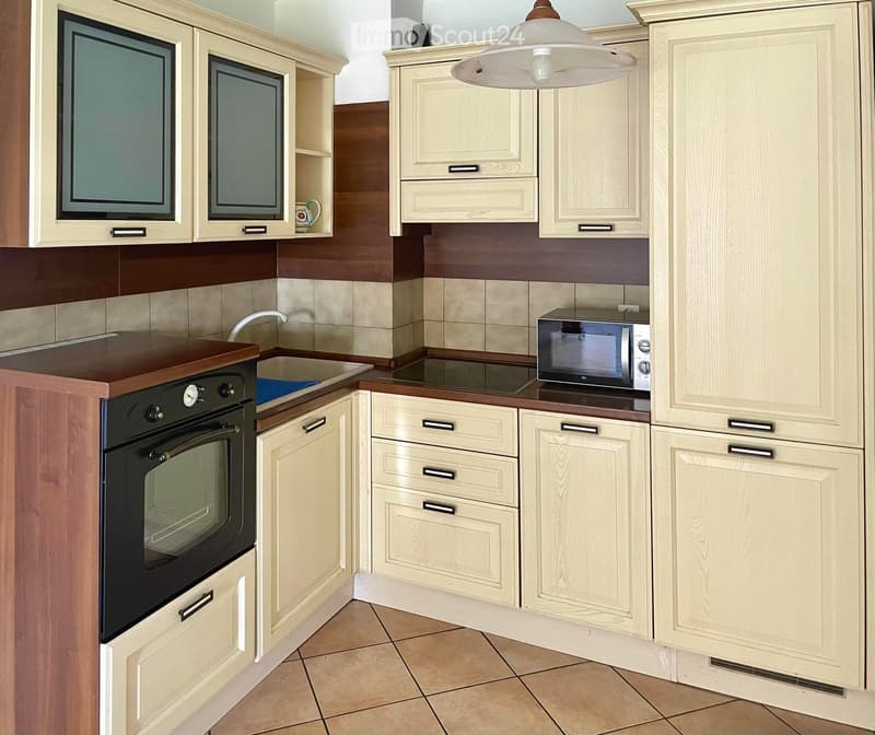 Modern kitchen with light wood cabinets, stainless steel appliances, and a central island with a dark countertop.