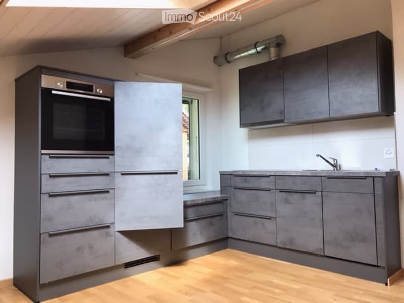 Modern kitchen with grey cabinets, wooden flooring, built-in oven, and a sink with a faucet.