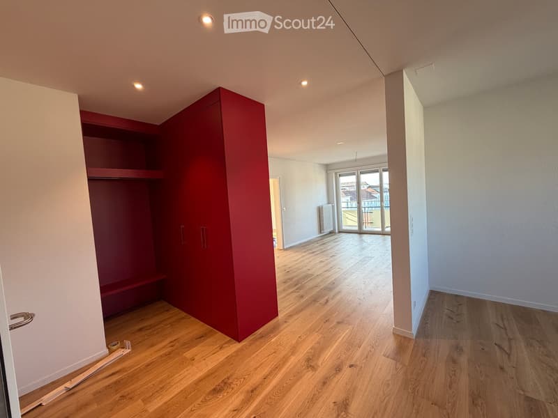 Empty room with wooden flooring, white walls, and a red closet. The room has a large window with a view and recessed lighting.