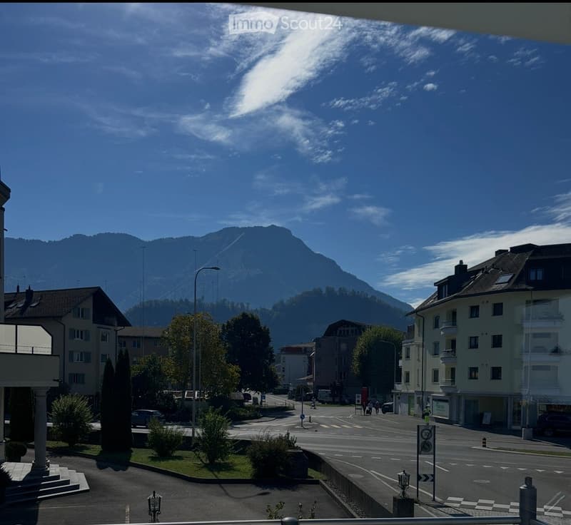 A scenic view of a town with buildings, trees, and a mountain in the background under a clear blue sky.