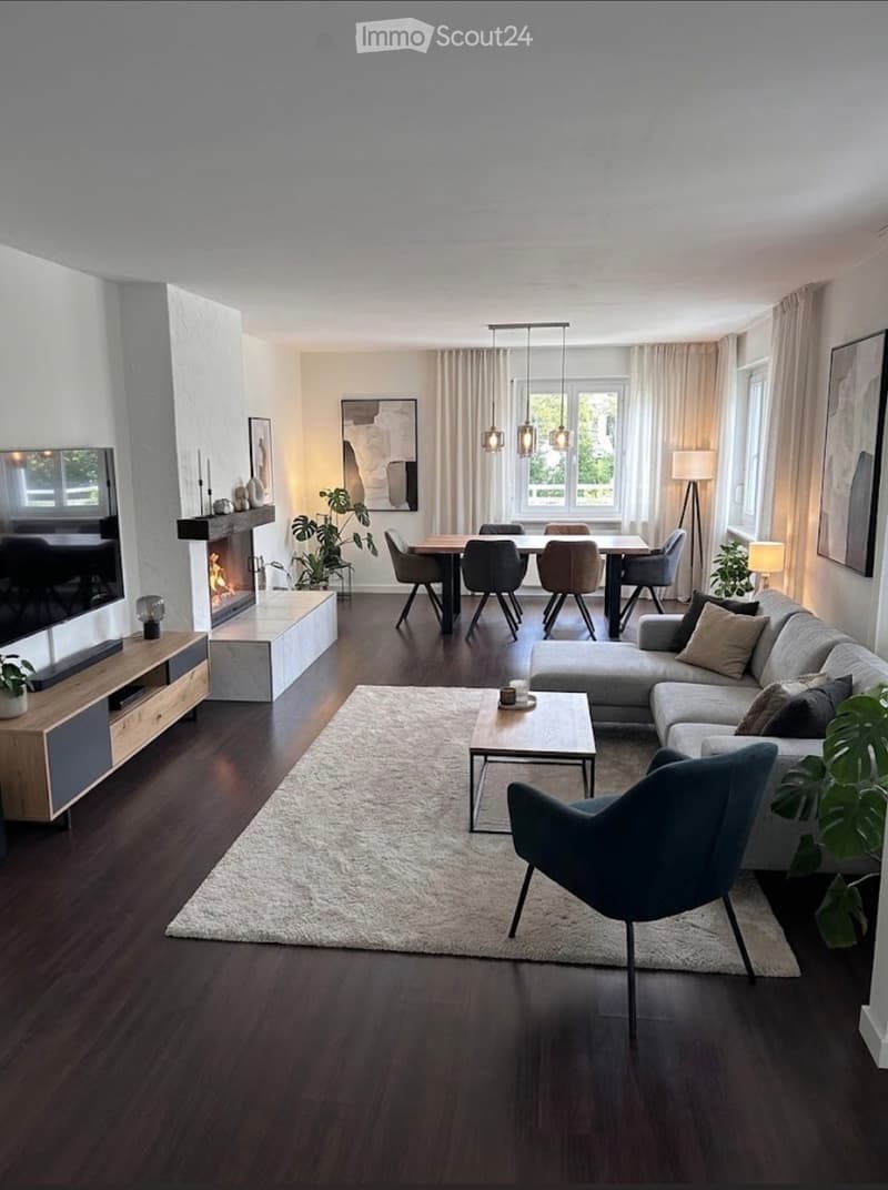 Modern living room with a sectional sofa, coffee table, dining area, fireplace, and large windows with curtains.
