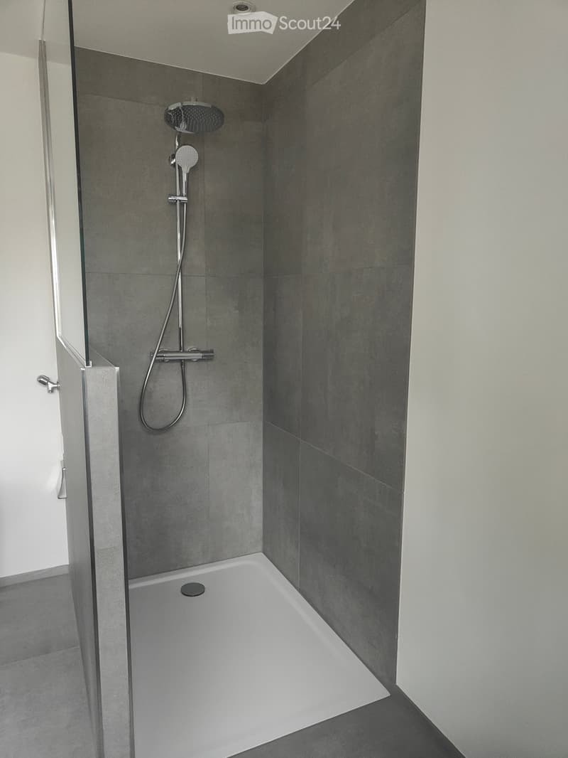 Modern shower room with gray tiled walls, shower head, white base floor, and open door