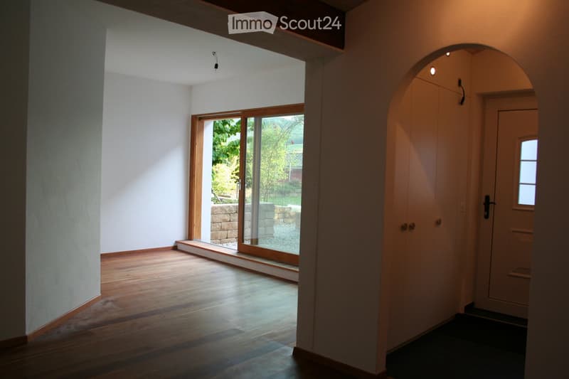 Bright, minimalist hallway with wooden flooring, white walls, and a large sliding glass door leading to a garden area.
