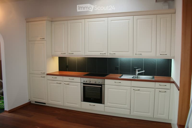 Modern kitchen with white cabinets, wooden countertops, and stainless steel sink and oven.