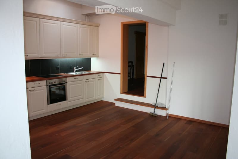 Modern kitchen with white cabinets, wooden countertops, and a dark backsplash. Features a sink, faucet, and oven. Wooden floor and a small step leading to another room.