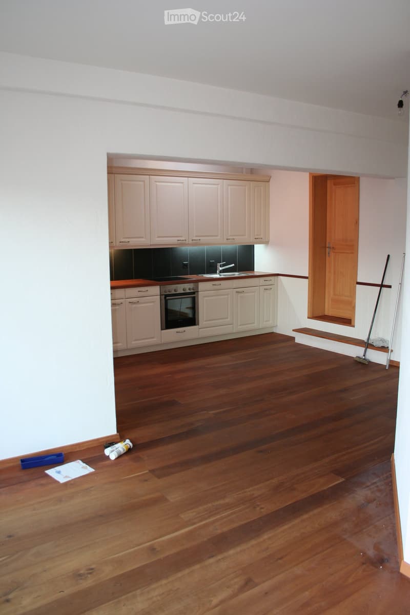 Empty kitchen with light-colored cabinets, wooden flooring, and a black backsplash. No furniture or appliances are present.