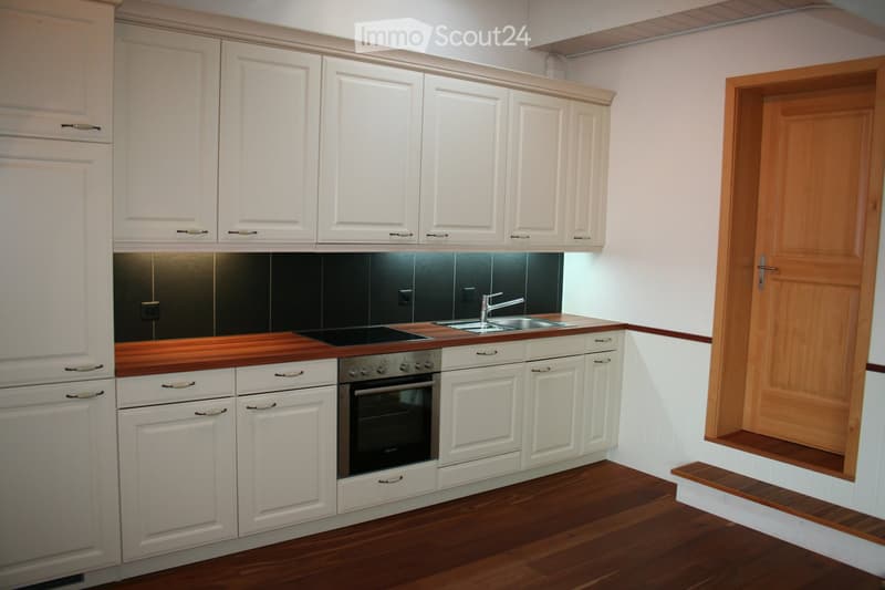 Modern kitchen with white cabinets, wooden countertop, stainless steel sink and faucet, built-in oven and stove, and wooden flooring.