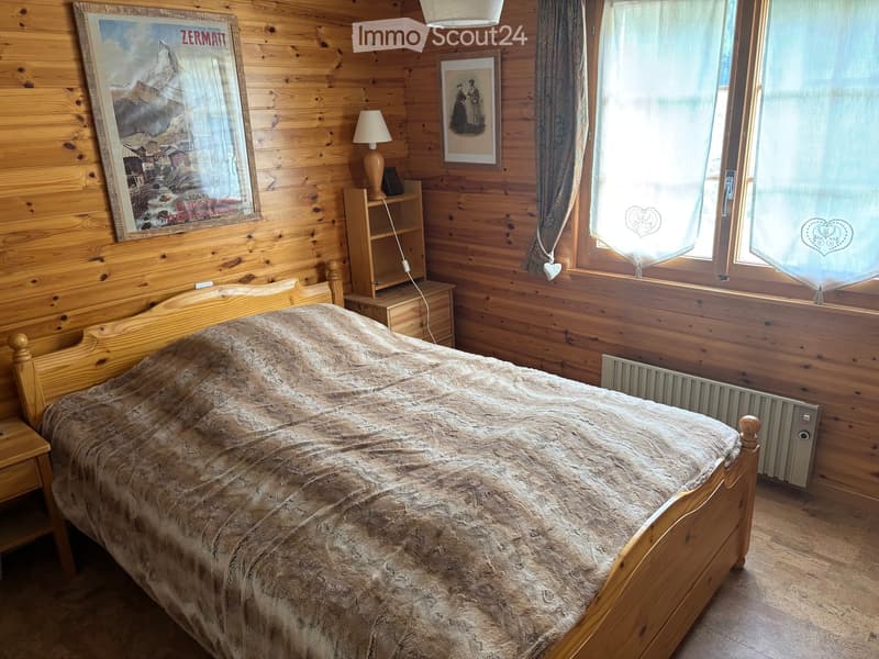 Cozy wooden bedroom with a large bed, nightstand, lamp, and framed pictures on the wall.