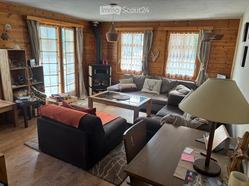 Cozy living room with wooden walls, a fireplace, a large sofa, coffee table, and a wooden table with a lamp.