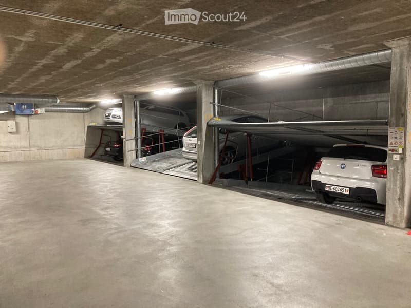 Underground parking area with cars on parking ramps, ceiling lights