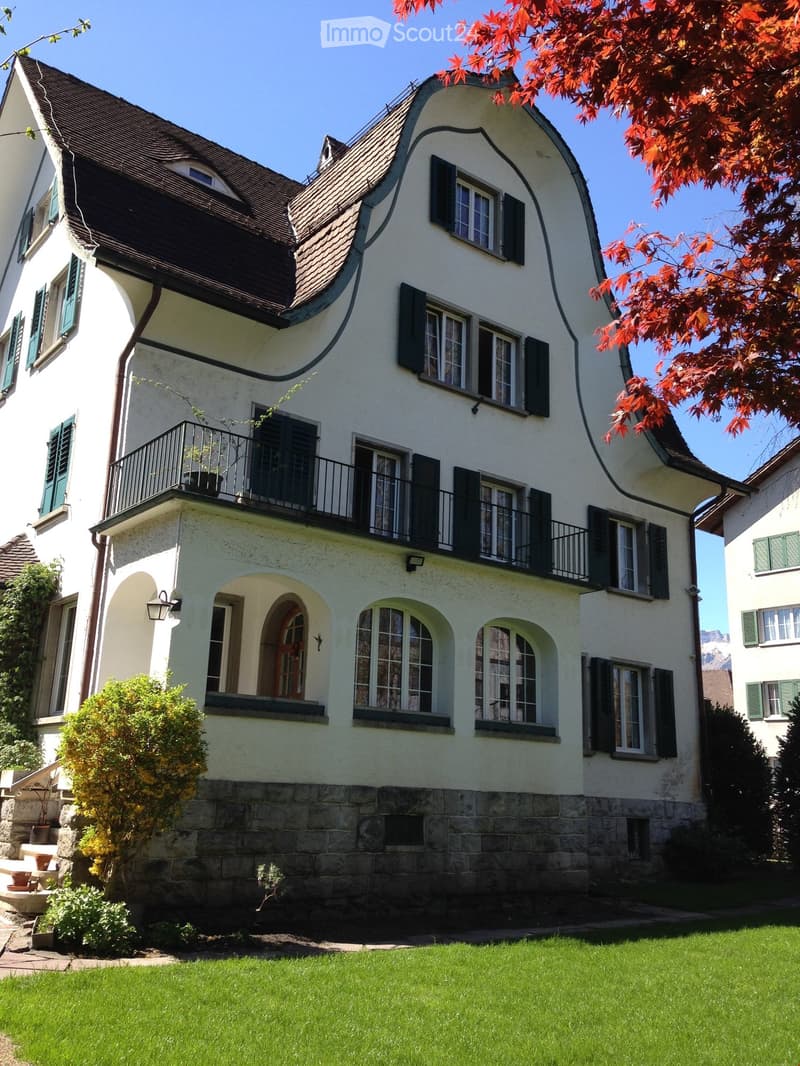 3 story house, white exterior, brown roof, green shutters, balcony, front yard with green grass, multiple windows