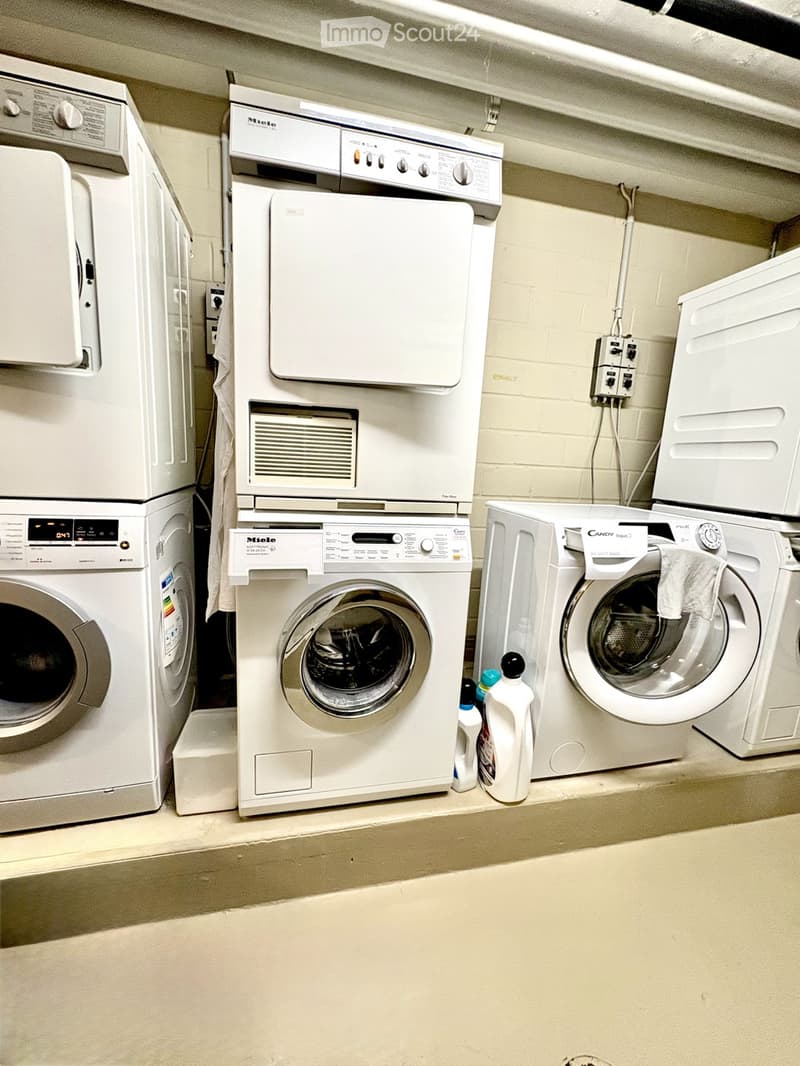 A well-organized laundry area with multiple washing machines, a dryer, and a dishwasher, all neatly arranged against a tiled wall.