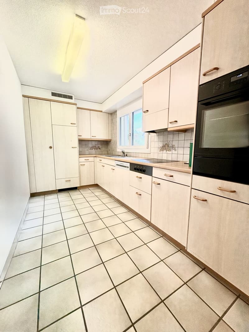 Bright kitchen with white tiled floor, light-colored cabinets, sink, dishwasher, and oven. Natural light from a window illuminates the space.