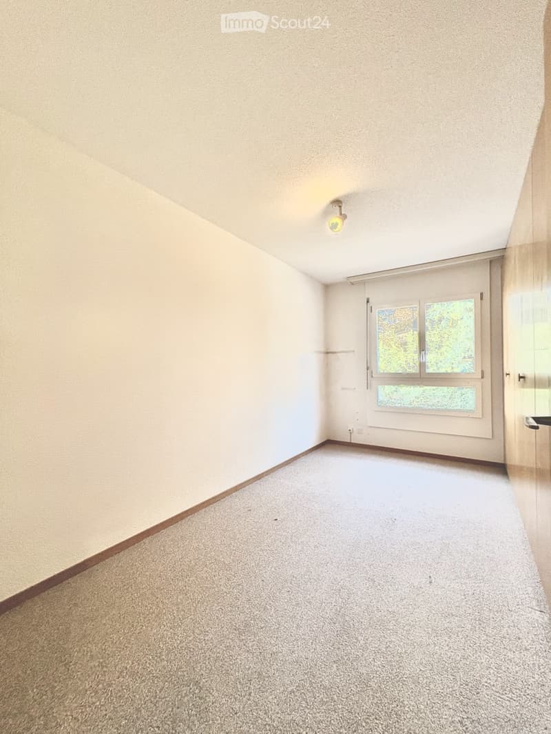 Empty room with beige walls, carpeted floor, and large windows with blinds. No furniture or equipment present.