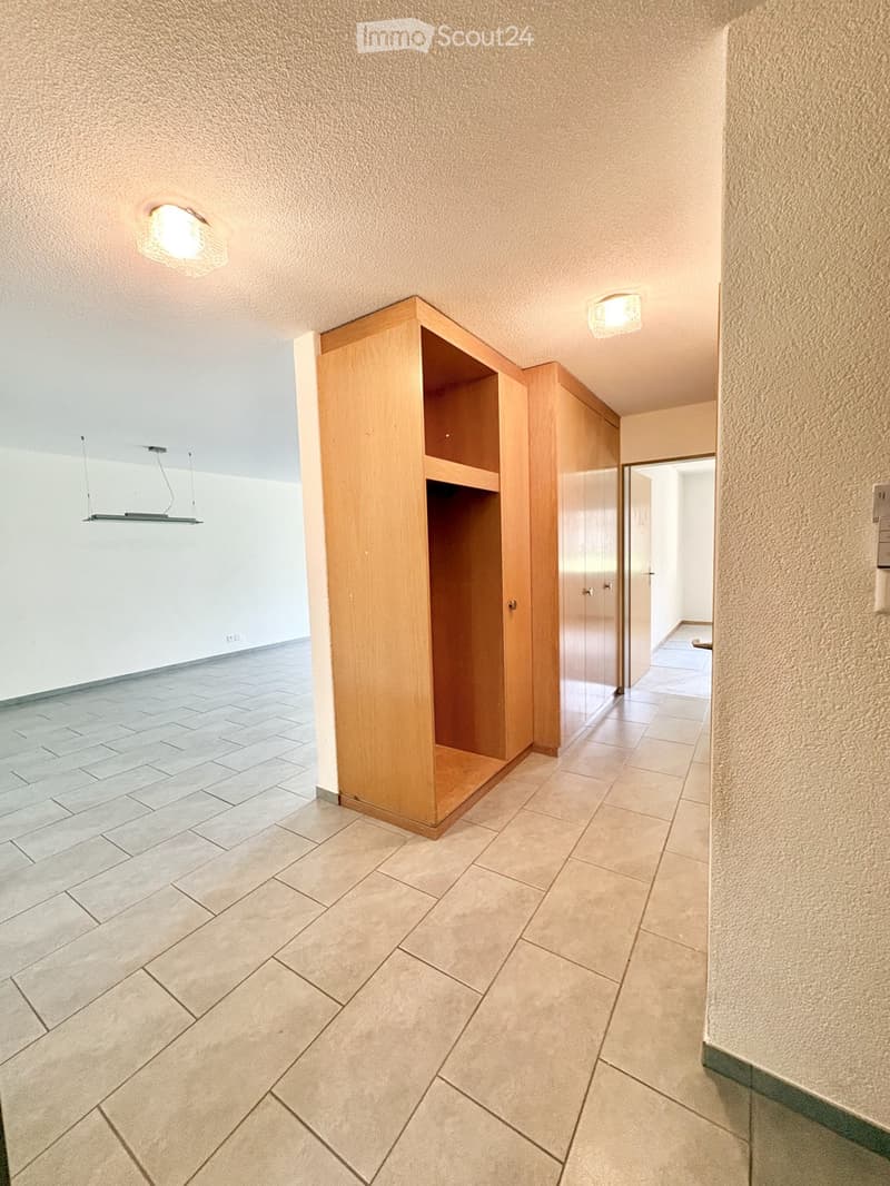 Empty hallway with tiled floor, wooden built-in storage unit, recessed ceiling lights, and a visible doorway leading to another room.