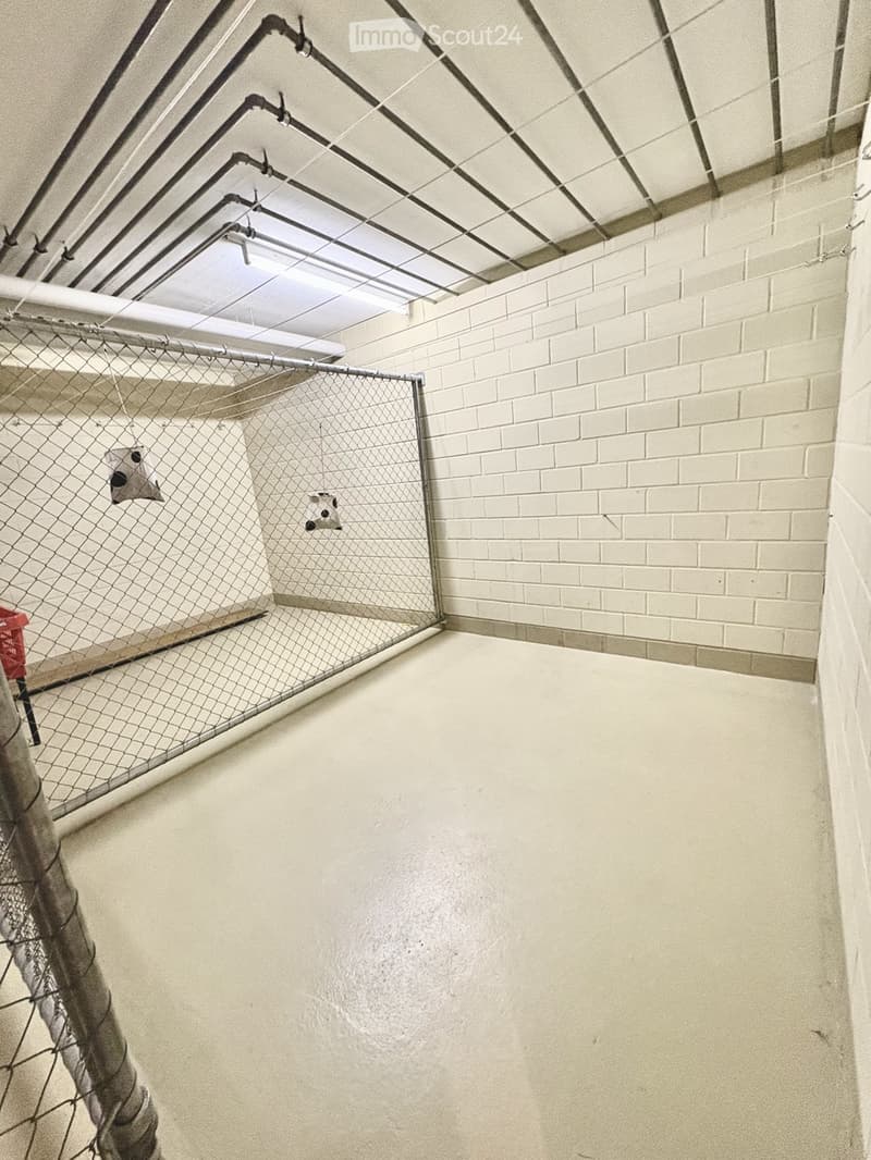An empty room with white brick walls, a metal fence, and exposed pipes and wiring on the ceiling.