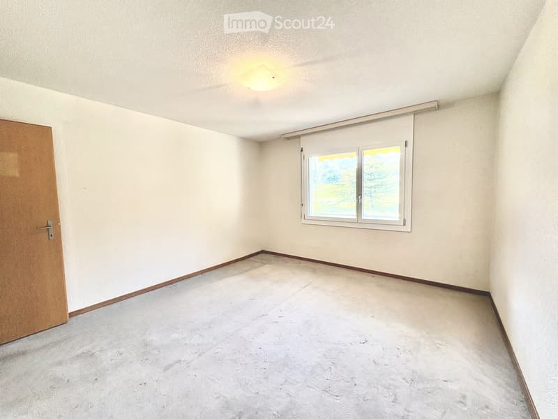 Empty room with light-colored walls, carpeted floor, a single window with blinds, and a wooden door.