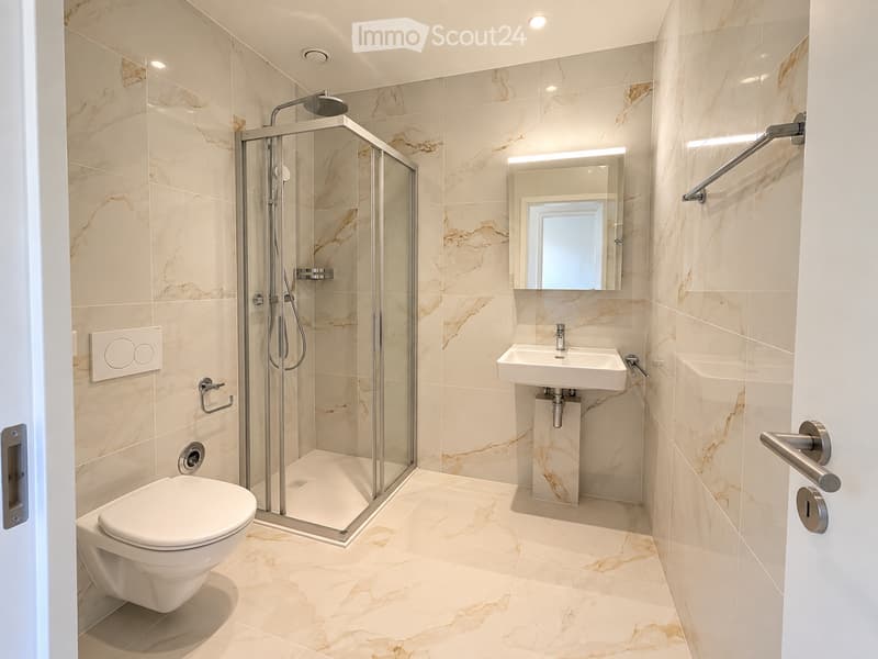 Modern bathroom with marble tiles, a glass-enclosed shower, a toilet, a sink with a mirror, and built-in lighting.