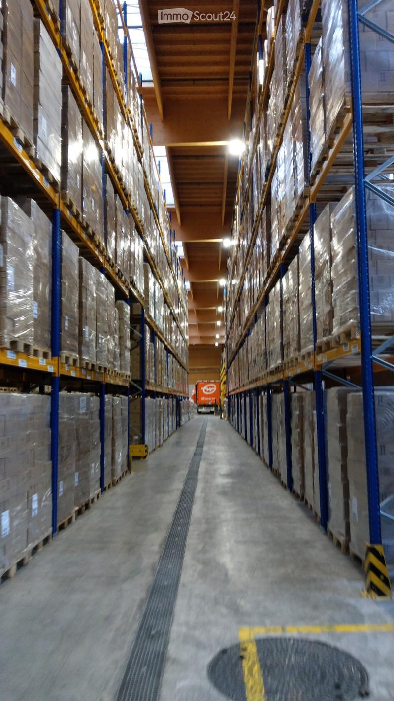 A large warehouse with high ceilings, metal shelving units filled with boxes and pallets, and a concrete floor.