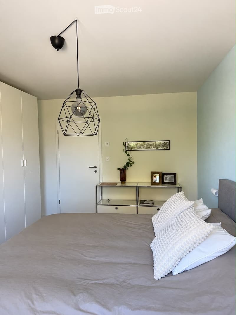 Modern bedroom with a large bed, nightstand, geometric pendant light, and decorative items on the nightstand.