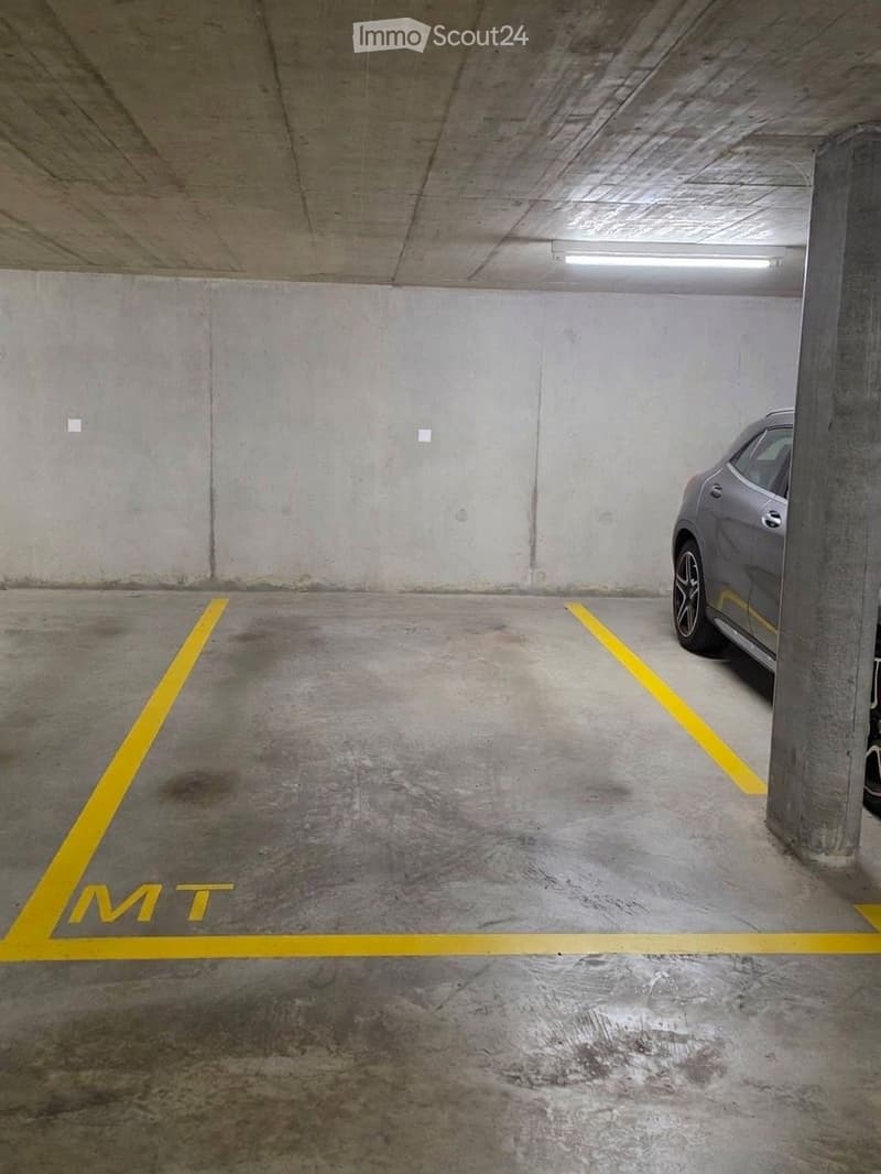 Underground parking space with concrete walls and floor, marked parking spots, and one parked car visible.