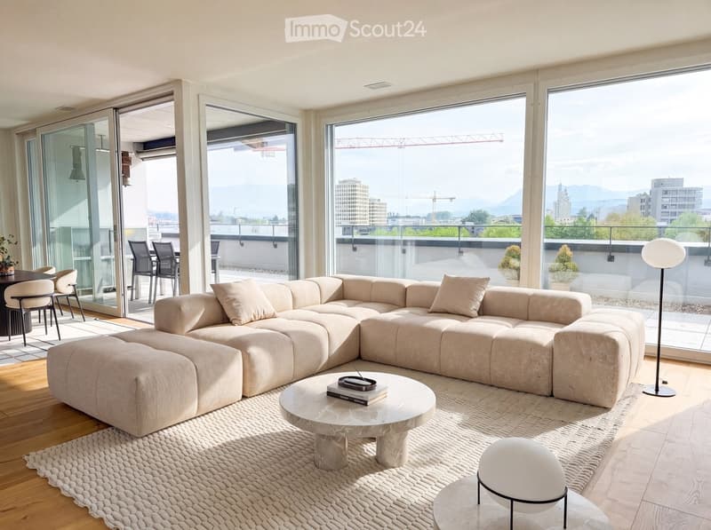 Modern living room with large windows offering a city view, featuring a beige sectional sofa, a round marble coffee table, a floor lamp, and a dining area with chairs and a table.