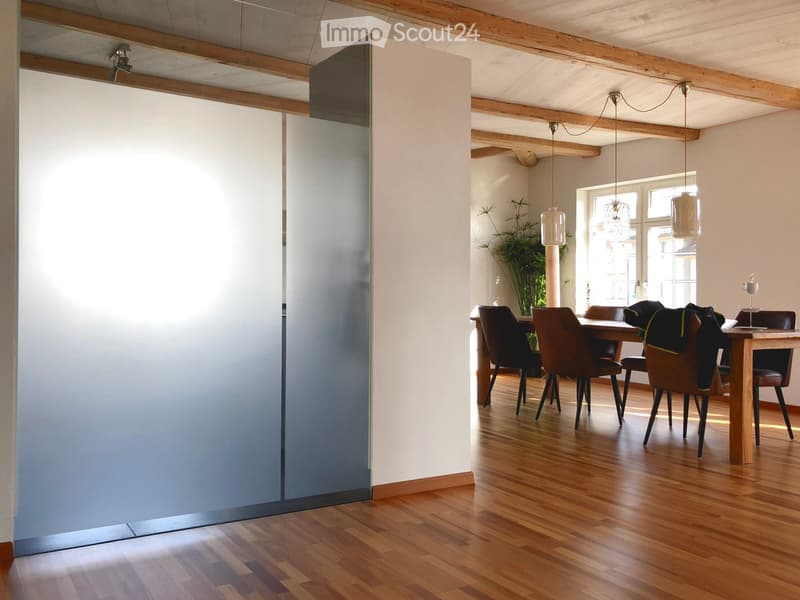 Dining area with wooden floor, modern pendant lights, dining table with chairs, and a plant in the corner.