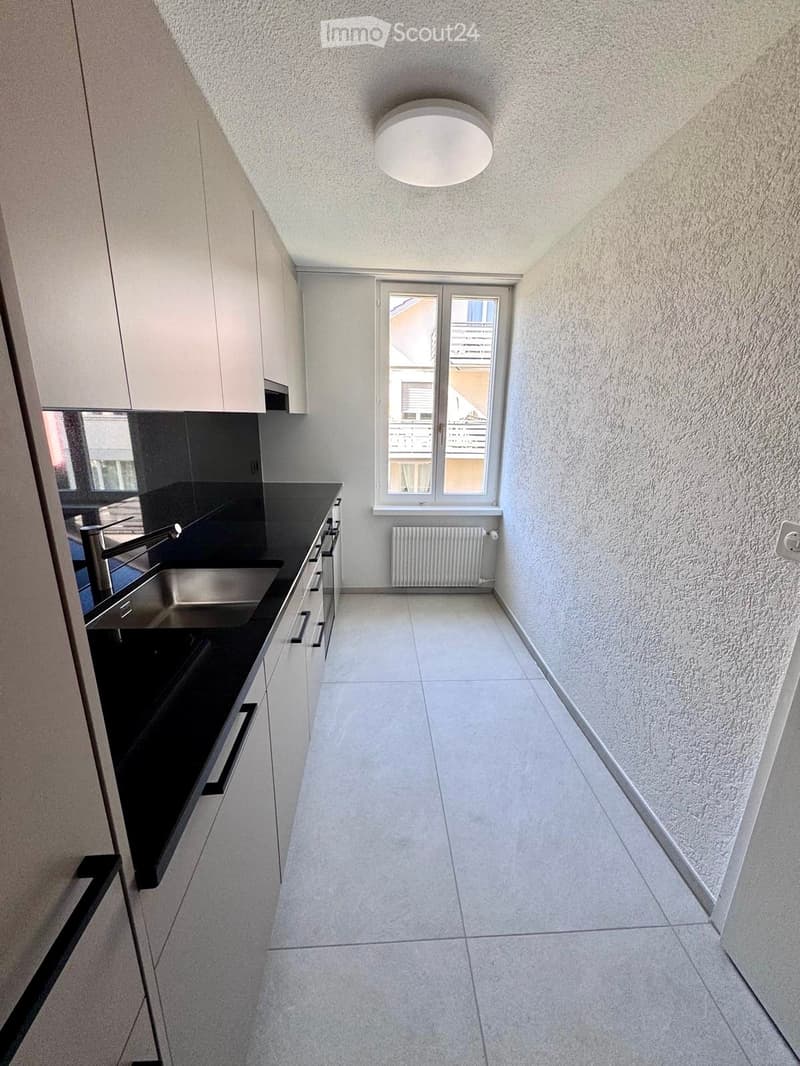 Modern kitchen with white cabinets, black countertops, stainless steel sink, and a window overlooking a balcony.