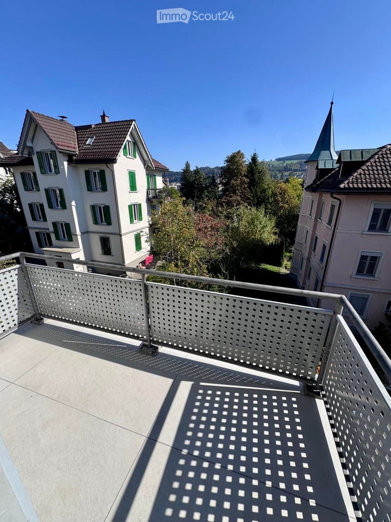 Balcony with metal railing, overlooking a residential area with houses, trees, and a church spire in the background.