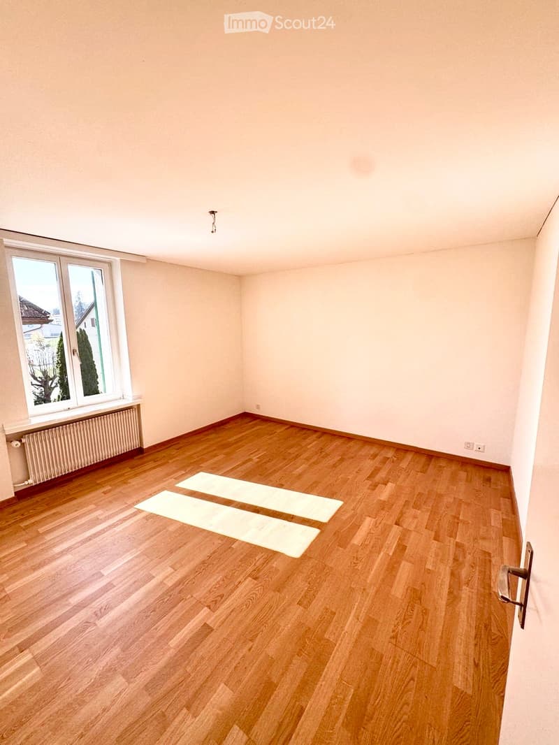 Empty room with wooden flooring, large window with view, radiator, and three yoga mats placed on the floor.