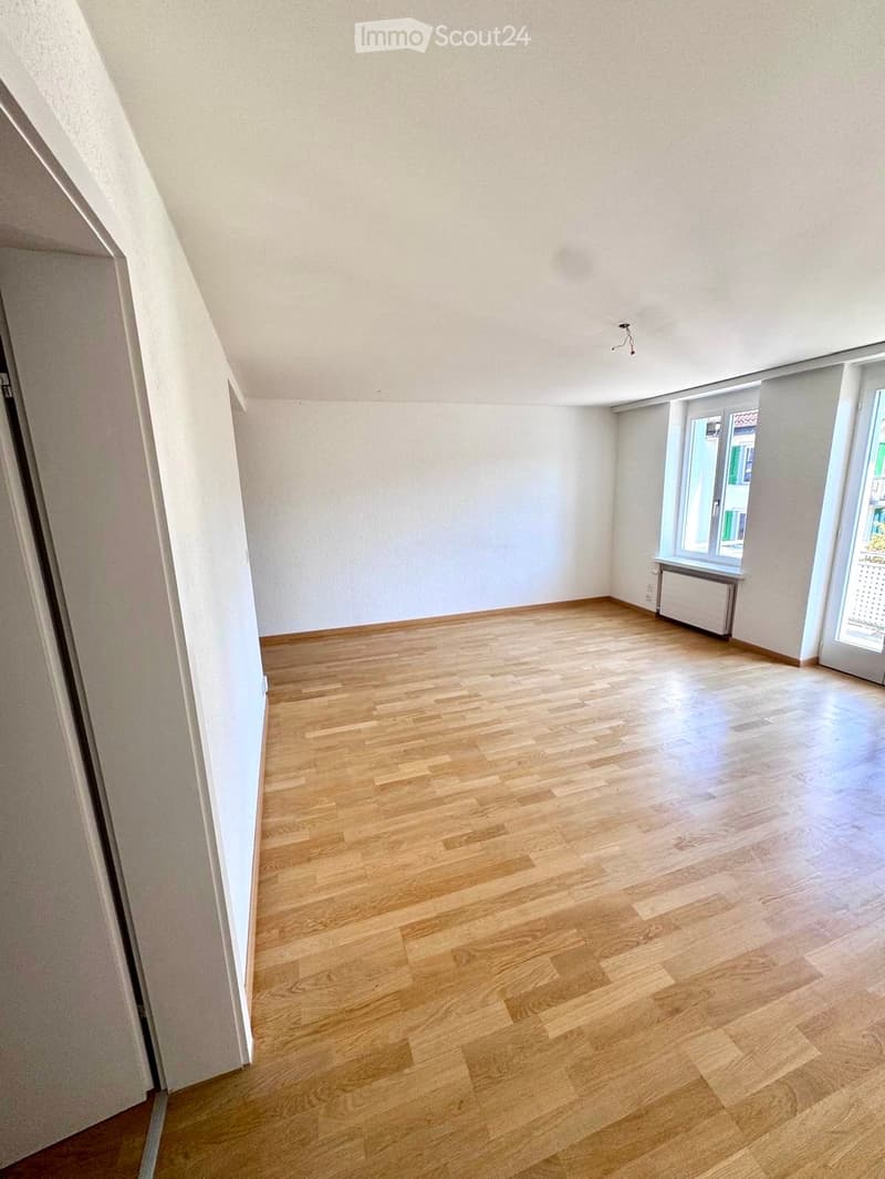 Empty room with wooden flooring, white walls, and large windows allowing natural light. No furniture or equipment is present.