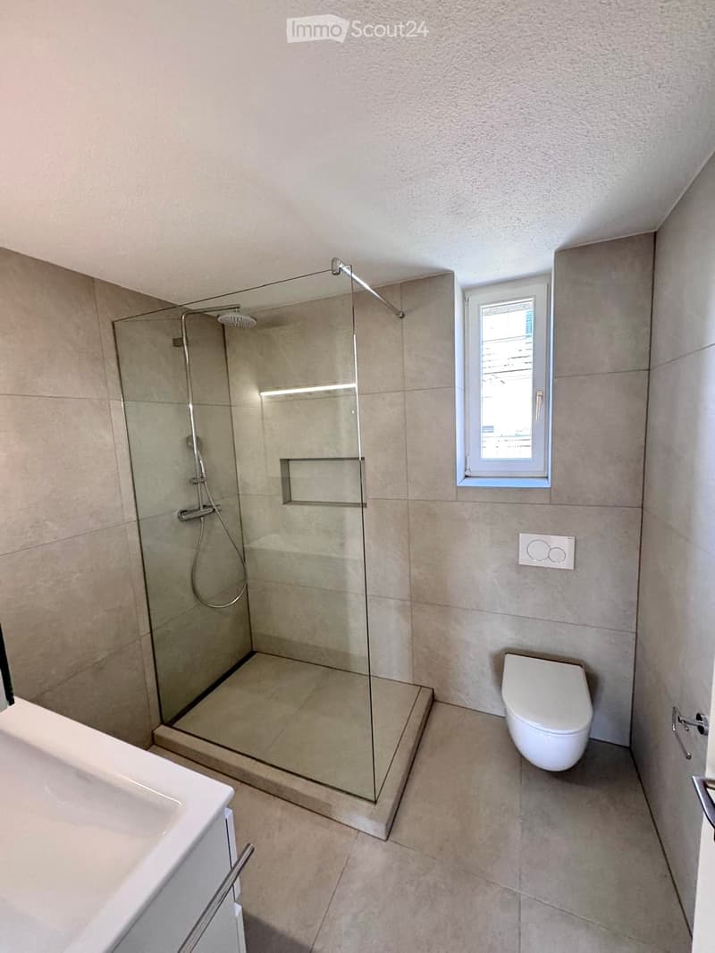 Modern bathroom with a glass-enclosed shower, bathtub, toilet, and a small window providing natural light.