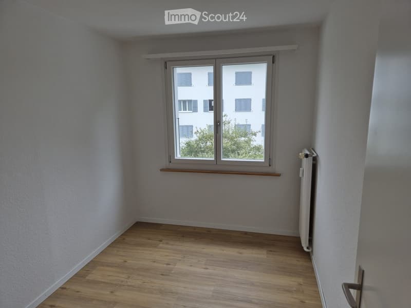 empty room with wooden floor, white walls, radiator, window