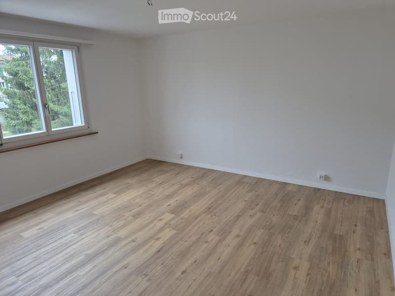Empty room, hardwood floors, white walls, two power outlets on the walls, large window with white frame