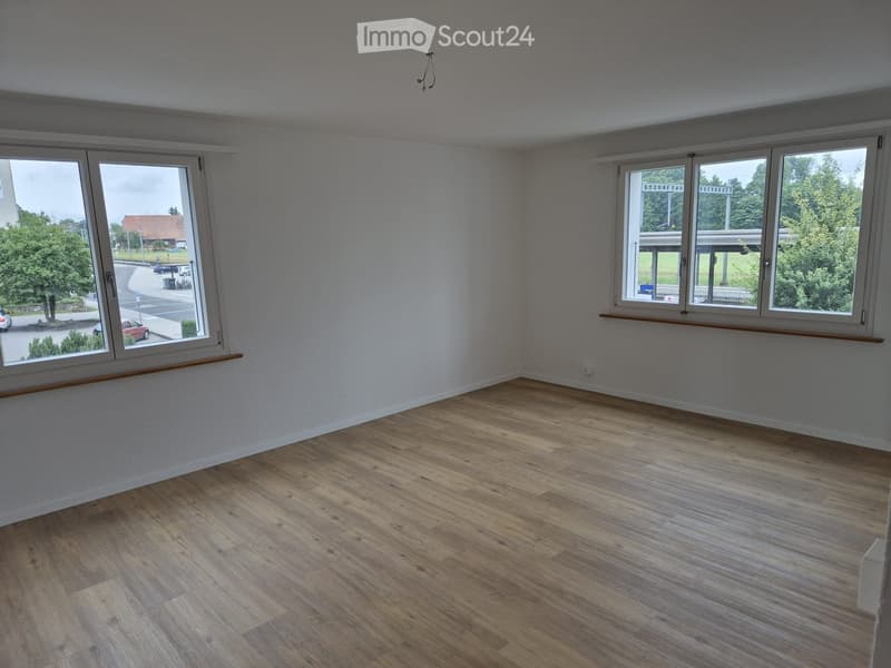 Empty room with wooden floors, white walls, large windows, street view