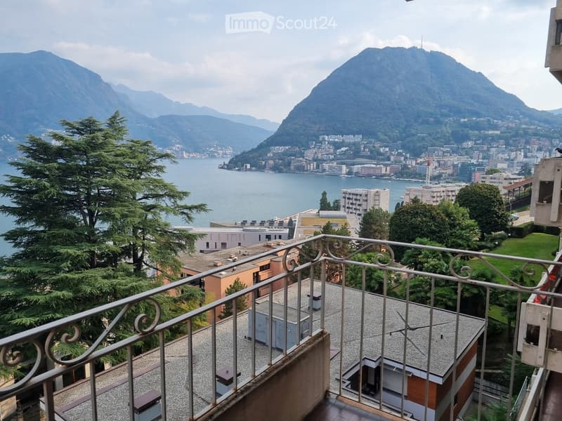 Balcony overlooking a scenic lake and mountain landscape, with a metal railing and tiled floor.