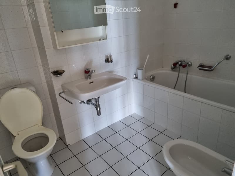 Bathroom with white tiled walls and floor, featuring a toilet, sink, bathtub, and a mirror above the sink.