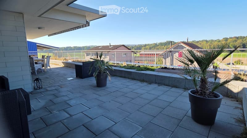 Modern balcony with tiled floor, outdoor furniture, potted plants, and a scenic view of the countryside.