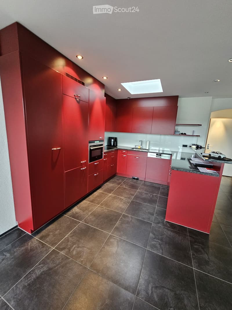 Modern kitchen with red cabinets, dark tiled floor, and built-in appliances including an oven, sink, and dishwasher.