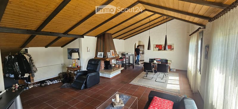 Living room with exposed wooden beams, fireplace, sofa, chairs, table, and hanging pendant lights.