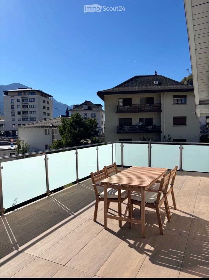 Balcony with wooden table and chairs, glass railing, and scenic mountain view.