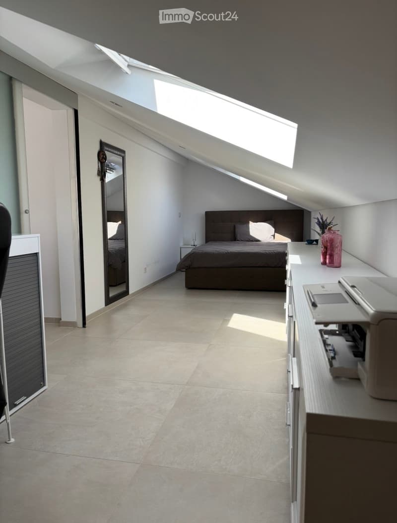 Modern attic bedroom with skylight windows, tiled floor, bed with dark headboard, nightstand, mirror, and decorative vase.