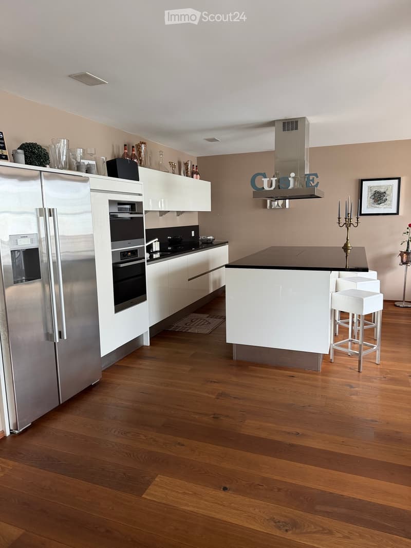 Modern kitchen with white cabinets, stainless steel appliances, wooden flooring, and a central island with bar stools.
