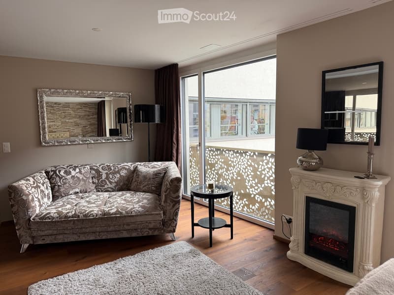 Modern living room with a patterned sofa, a small round coffee table, a decorative fireplace with an electric fire, and large windows with a balcony view.