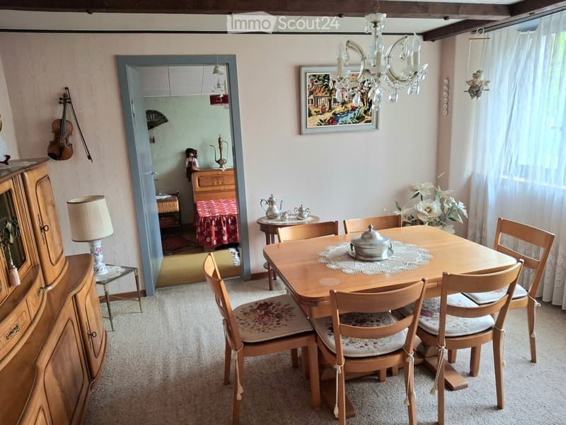 Dining room with a wooden dining table, six chairs, a cabinet, a lamp, a chandelier, and a mirror leading to another room.
